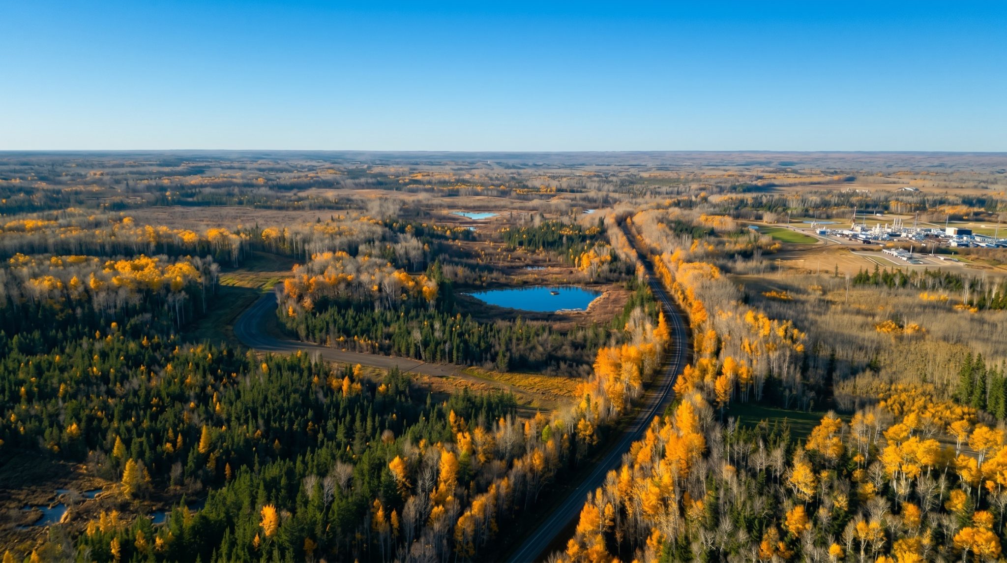 Aerial view of the Greenview Industrial Gateway area in autumn, with boreal forest, wetlands and a road running toward an existing gas plant